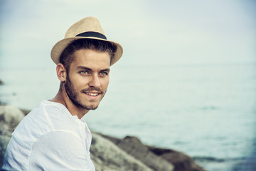 Handsome Young Man in Trendy Attire, on a Beach in a Sunny Summer Day, Wearing a White Shirt and Straw Hat