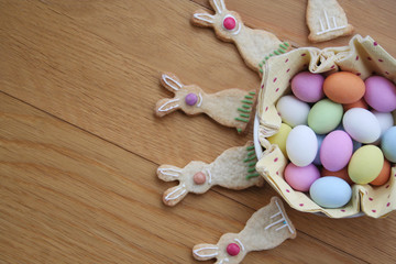 Decorated Easter cookies in shape of bunny with multi colored chocolate eggs on wooden table
