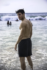 Fototapeta na wymiar Handsome young man standing on a beach in Phuket Island, Thailand, shirtless wearing boxer shorts, showing muscular fit body