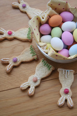 Decorated Easter cookies in shape of bunny with multi colored chocolate eggs on wooden table