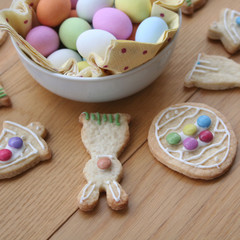 Decorated Easter cookies in shape of bunny with multi colored chocolate eggs on wooden table
