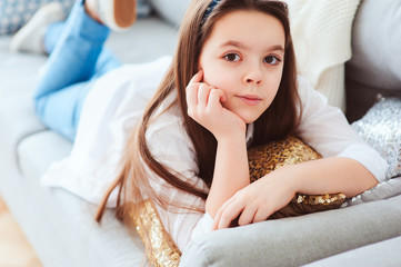 happy kid girl close up portrait. Preteen relaxing at home on cozy couch in white shirt and casual...