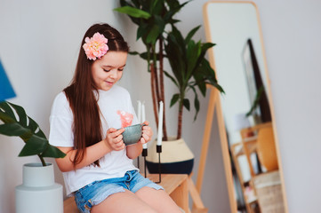 happy preteen girl resting at home, sitting with cup of hot tea with houseplants on backgroung in stylish modern interior