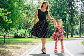 Mother teaching daughter to ride on rollers. Cheerful young woman and cute little daughter ride on...