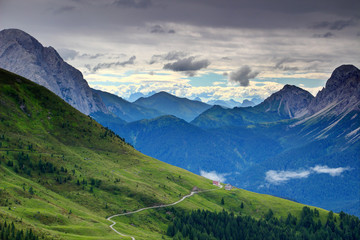 Grassy gentle slopes with dirt road and chalet in Alpi Carniche with Alpi Giulie in background, Monte Peralba, Crostis, Chiadin, Lastroni peaks, Cadore Carnia Belluno Veneto Northern Italy Europe