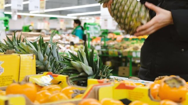 Woman chooses ripe pineapple in the store