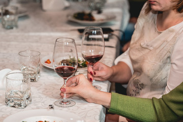 woman holds glass of red wine. people consider the color of the wine and try how it smells in different glasses