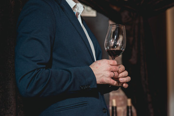 man in a blue suit with a skin disease holds glass of red wine. people consider the color of the wine and try how it smells in different glasses