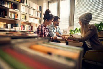 Concept of education, library, students and teamwork. Three productive young friends sitting in the library and studying for a test or an exam together from notes and the books.