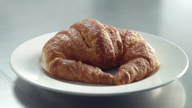 closeup of inox table and man's hand putting a dish with croissant on it in morning light