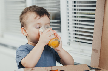 baby in the kitchen drinking orange juice and eating a large pizza