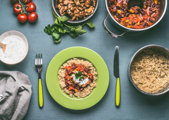 Healthy meal with quinoa, tomatoes beans sauce and fried chicken meat on kitchen table background with food pots bowls and cutlery , top view