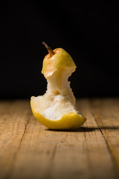 view of a piece of bitten pear, isolated, on old wooden table and black background