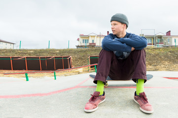 A teenage boy is sitting on a skateboard in the park. The concept of free time pastime for...