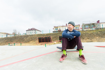 A teenage boy is sitting on a skateboard in the park and smiling. The concept of free time pastime for teenagers in the city