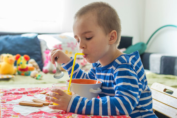 Little boy sitting at table and drinking orange juice using straw © Helios4Eos