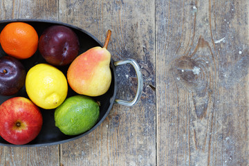 Mixed fruits of apples, lime, lemon, pears and plums in metal tray on wood table with copy space right