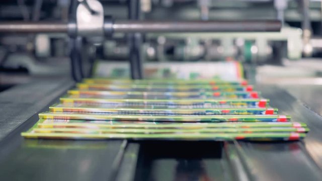 Portions of coloured journals are getting collected from a conveyor belt by a person