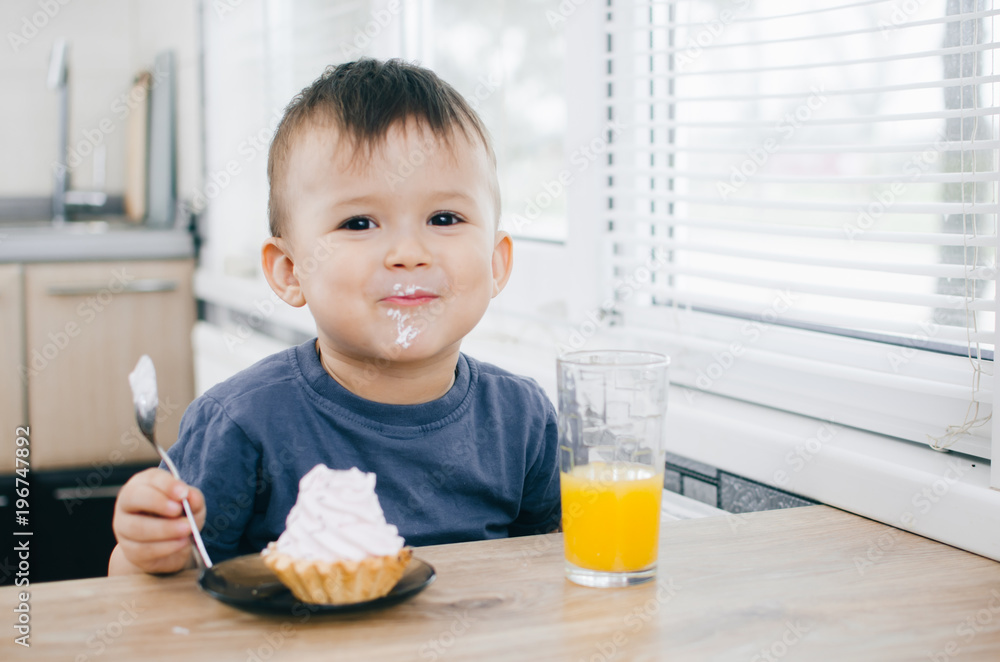 Wall mural the child in the kitchen eating a cake with cream is very appetizing, spoon