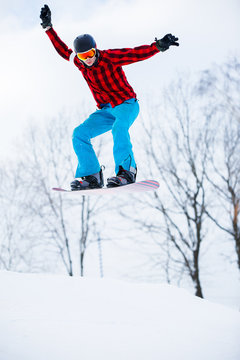 Photo of sportive man with snowboard jumping in snowy resort
