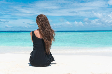 Woman sitting on beach with transparent water of ocean in Maldives