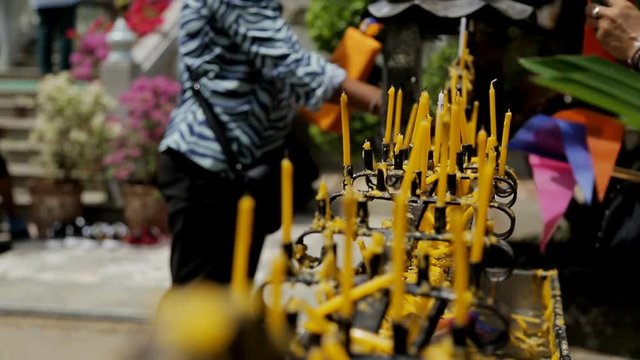 Rows of yellow slim candles, which are put into black holder ouside, close up. Candlestick is metal, black and beaten. Female tourist at the background is lighting her tool to place it near the others