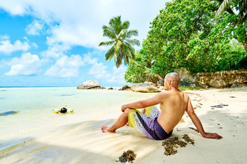 man tourist on tropical beach under palm tree, Anse a La Mouche,