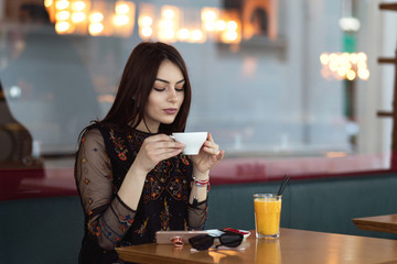 Beautiful young woman sitting at table in street cafe terrace enjoying a cup of coffee or cappuccino and a glass of fresh orange juice. 