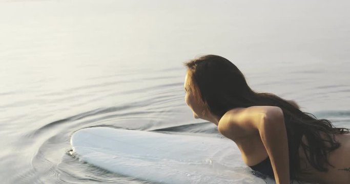 sexy fit sporty brunette girl or tanned woman or female surfer lying on surfboard, getting ready to surf. summertime travel, vacation. ocean or sea around