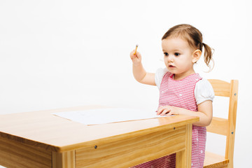 Naklejka premium Small preschool child at school desk with pencil and one hand raised , isolated on white