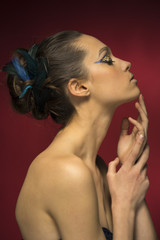 Portrait of a beautiful young girl with a chignon decorated with feathers and a gold and blue makeup