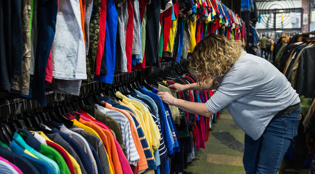 Woman browsing and searching through t-shirts in a thrift store