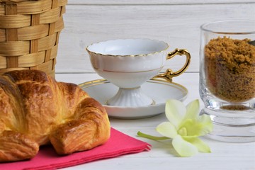 An empty coffee cup on a saucer, Croissant, item basket, flower, brown sugar on a wooden painted background