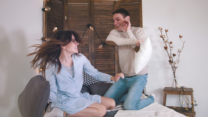 Happy cheerful loving couple having a fight in bed, girl tickling guy
