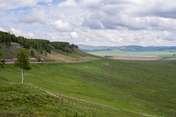 Naklejka premium The road runs along the foot of the mountain past the green valley, in the spring.