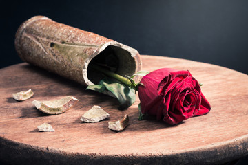 red roses in ceramic broken cylinder shape fell vase on the old wooden table with dark background