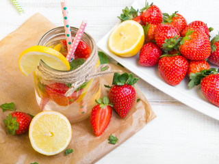 Mineral  water with fresh strawberries, lemon  and mint in jar on a white wooden background, copy space