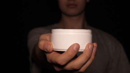 Cream for hands (face), in a white jar, on a black background.