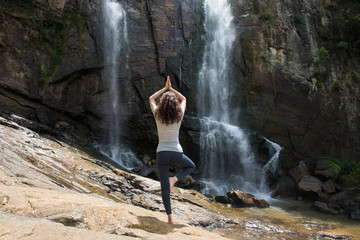 Fototapeta premium Young woman in yoga pose staying in front of waterfall