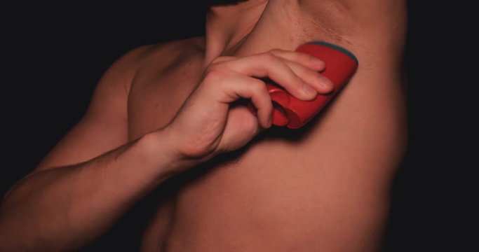 The body of a man, a man holds in his hand a red deodorant for the armpits, a black background.