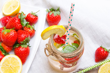 Mineral  water with fresh strawberries, lemon  and mint in jar on a white wooden background, copy space