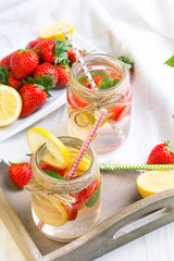 Mineral  water with fresh strawberries, lemon  and mint in jar on a white wooden background, copy space