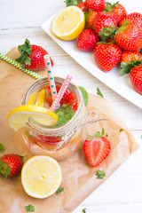 Mineral  water with fresh strawberries, lemon  and mint in jar on a white wooden background, copy space