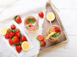 Mineral  water with fresh strawberries, lemon  and mint in jar on a white wooden background, copy space