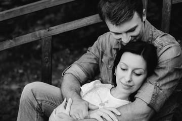 Young pretty happy couple sitting on wooden stairs in the park. Man and woman dating and flirting outdoors.