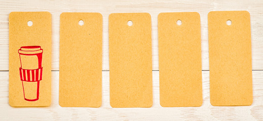 five recycled paper tags with cute pink drawing of coffee cup and blank on white wooden background
