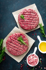 Fresh minced beef meat burgers with spices on dark background. Raw ground beef meat. Flat lay. Top view