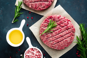 Fresh minced beef meat burgers with spices on dark background. Raw ground beef meat. Flat lay. Top view