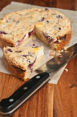 Top view, close up of a freshly baked, wedge of raspberry cream coffee cake, on a piece of parchment paper with a chef's knife on a wood cutting board