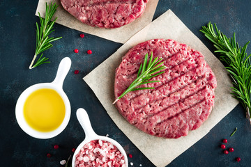 Fresh minced beef meat burgers with spices on dark background. Raw ground beef meat. Flat lay. Top view